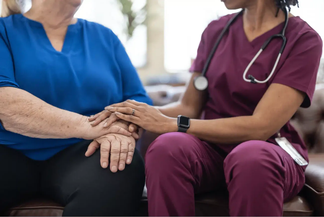 A hospice nurse holding the hands of an older woman during a home visit